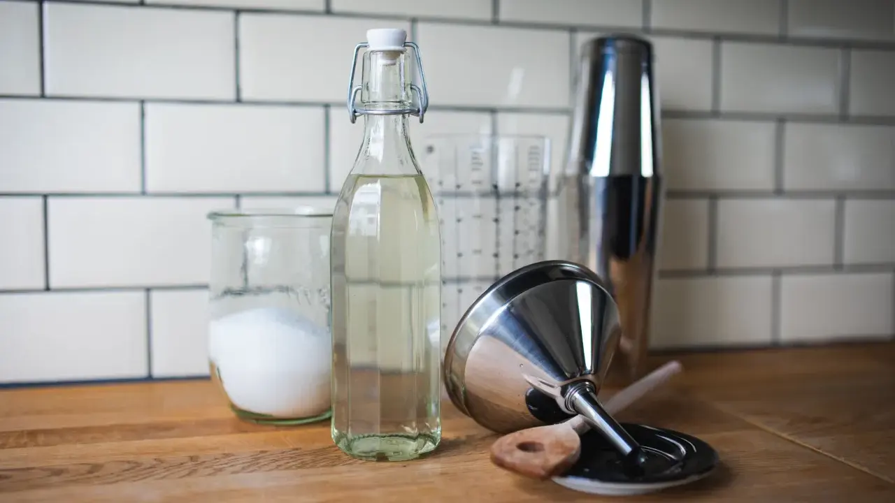 Zutaten für zuckersirup selber machen: Zucker in einem Glas, Sirup in einer Flasche, Cocktail-Shaker und Trichter.