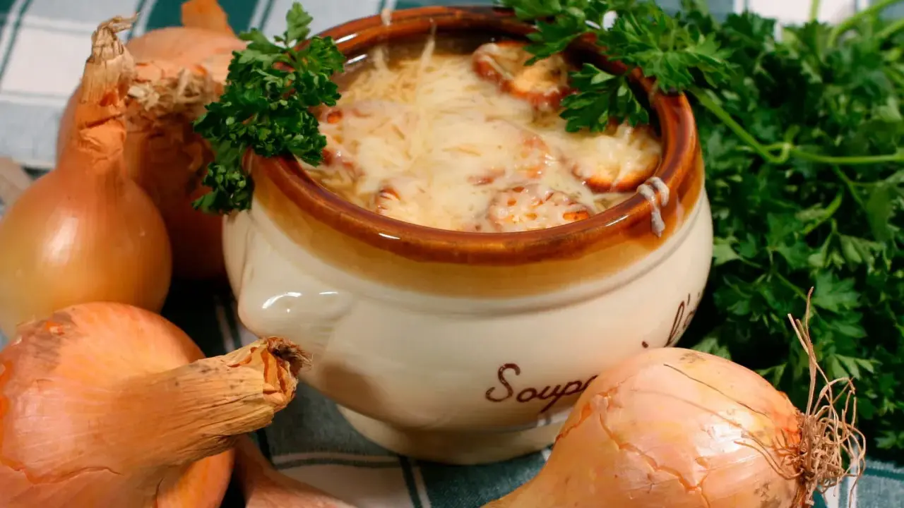 Un bol de soupe à l'oignon gratinée, un plat parisien réconfortant, entouré d'oignons frais et de persil.