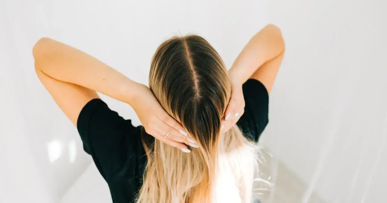 Kobieta z blond włosami, która delikatnie dotyka swojej głowy, jakby stosowała krople żołądkowe na włosy dla ich wzmocnienia.
