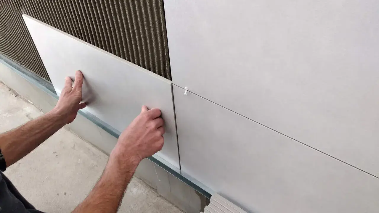 Ręce układają płytki 30x60 na ścianie, tworząc równą, nowoczesną powierzchnię. Widać klej i krzyżyki dystansowe.