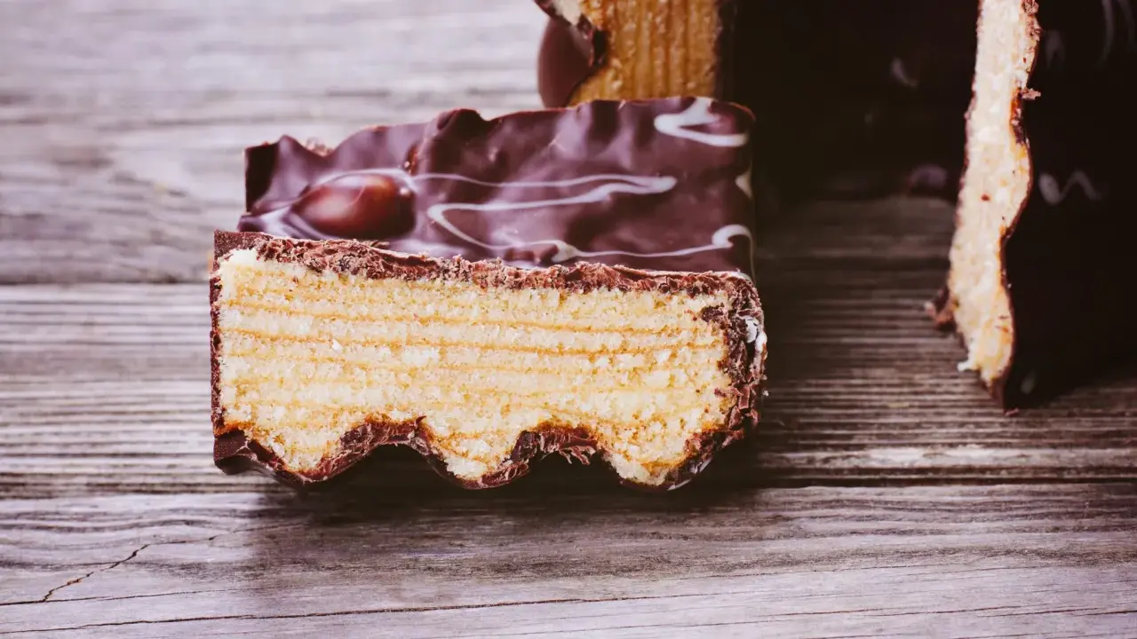Ein Stück Baumkuchen mit Schokoladenglasur und weißen Zuckerguss-Wirbeln, perfekt für ein Baumkuchen Rezept.