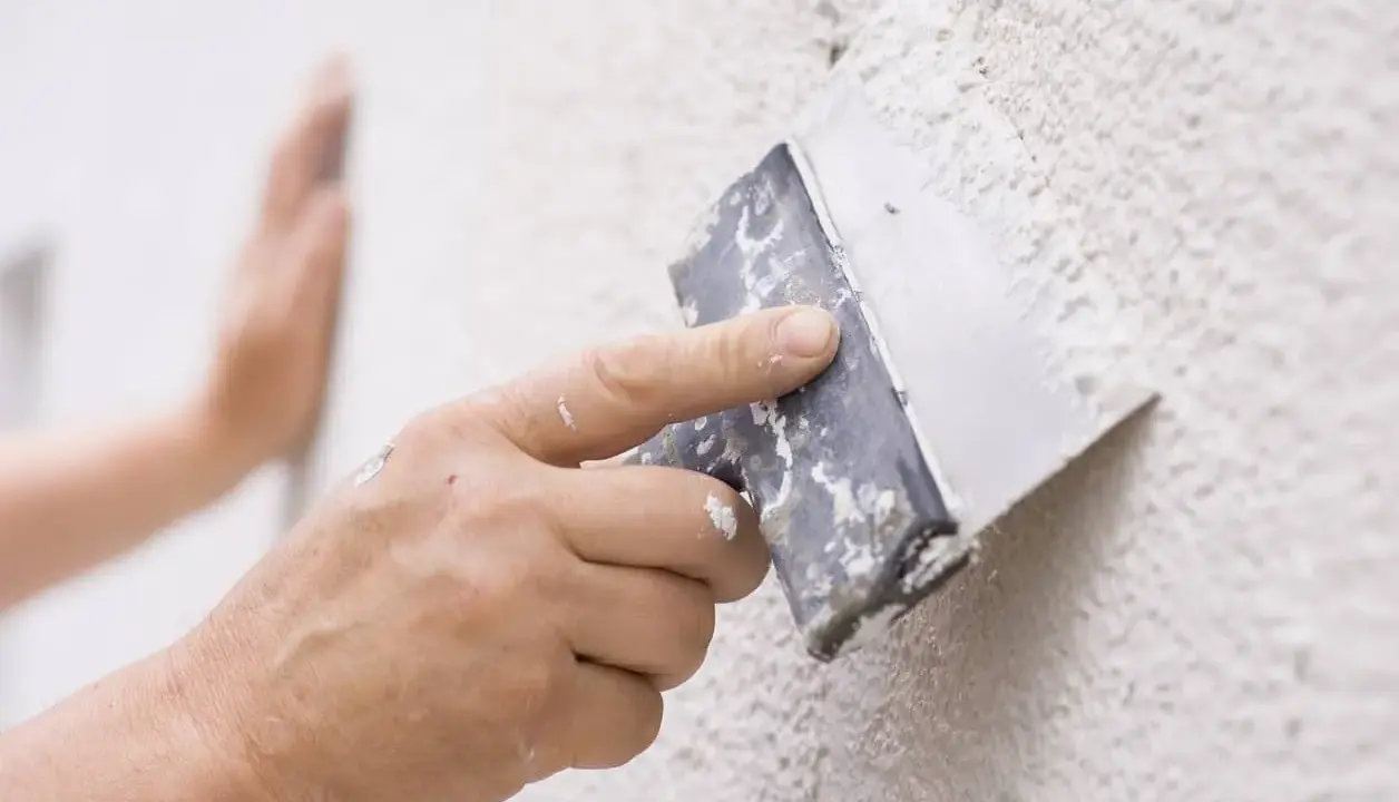 Mano aplicando masa con espátula para reparar gotele en pared.