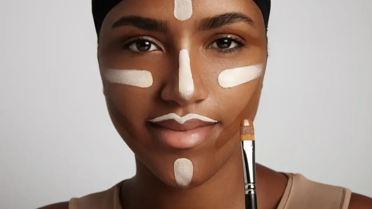 Mujer con líneas de maquillaje para **contouring cara**. Se ve un pincel en su mano.