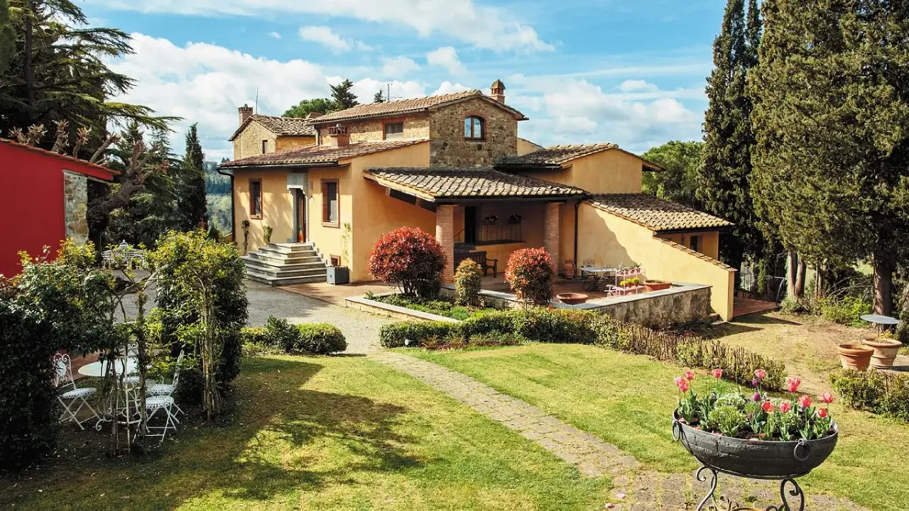 Un perfetto weekend in Toscana: villa con giardino fiorito, cipressi e un cielo azzurro con nuvole bianche.
