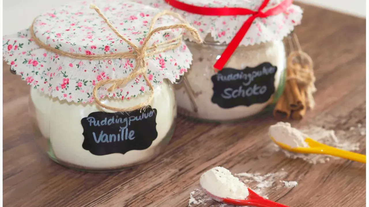 Zwei Gläser mit selbstgemachtem Puddingpulver (Vanille & Schoko) auf einem Holztisch, bereit für köstliche Desserts.