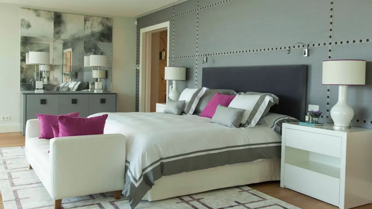Ideas para diseñar tu habitacion: cama moderna con detalles grises y rosas, mesitas blancas, sofá y espejo decorativo.