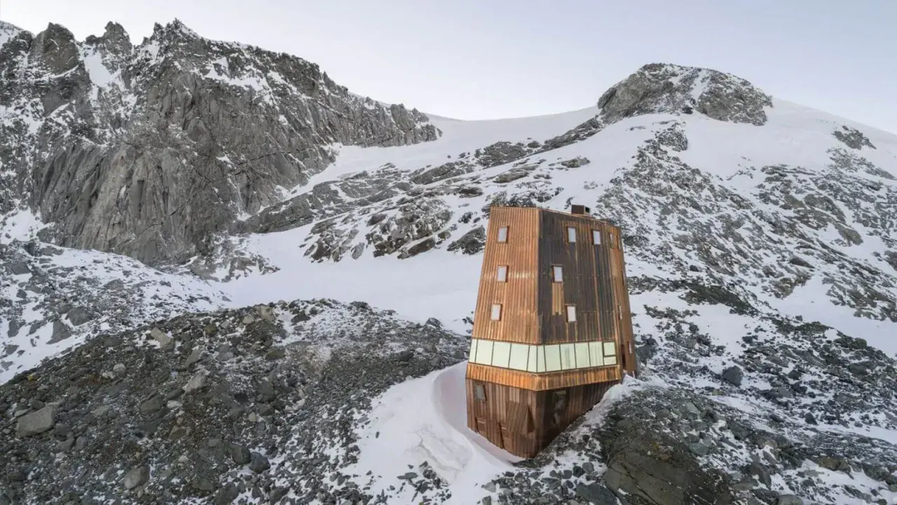 Il rifugio Sasso Nero, un'architettura moderna in legno, si erge solitario tra rocce e neve, dominato da imponenti vette montuose.