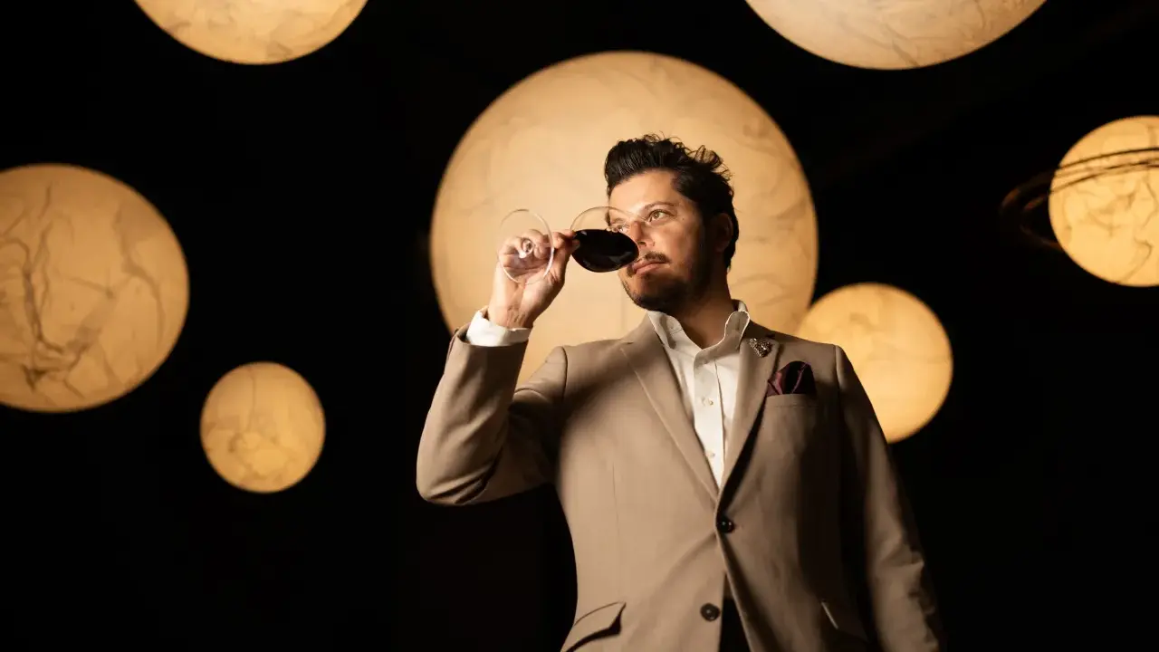 Un homme en costume déguste un verre de vin rouge, entouré de lumières rondes évoquant des planètes. Une dégustation qui rappelle la philosophie du vin biodynamique.