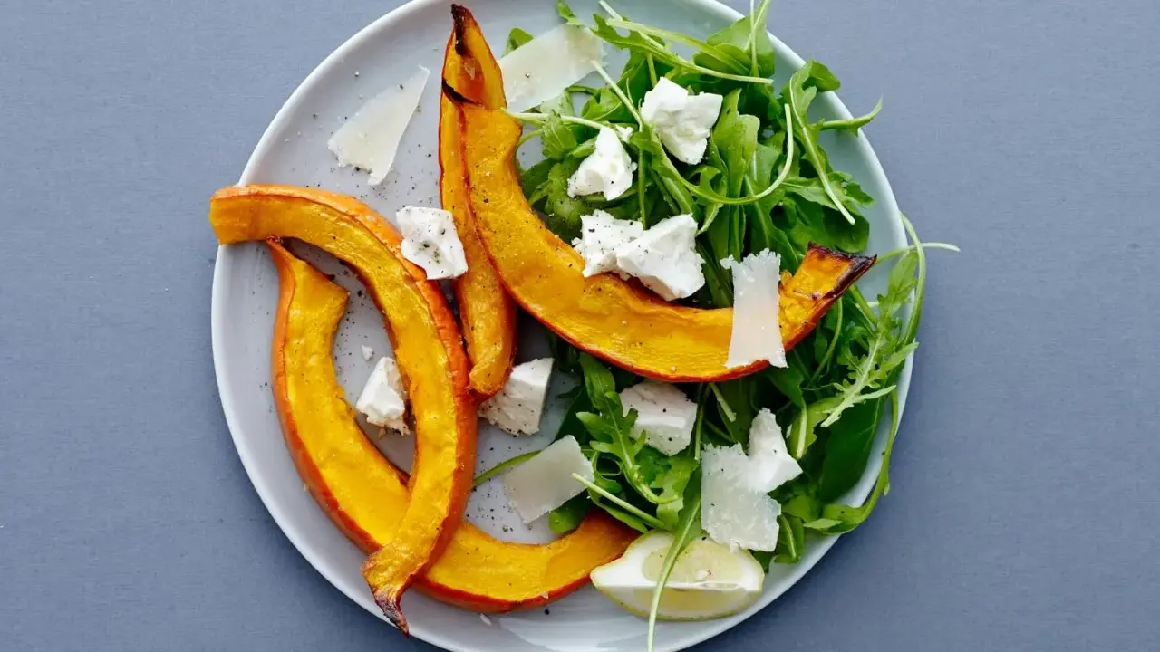 En härlig sallad med ruccola och fetaost, toppad med ugnsrostad pumpa och en citronskiva.