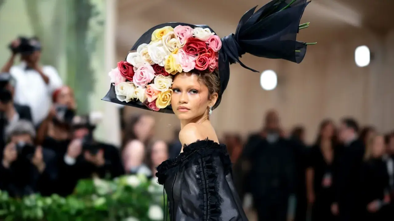 Zendaya stuns at the Met Gala in a dramatic black gown and a voluminous hat adorned with a cascade of colorful roses.
