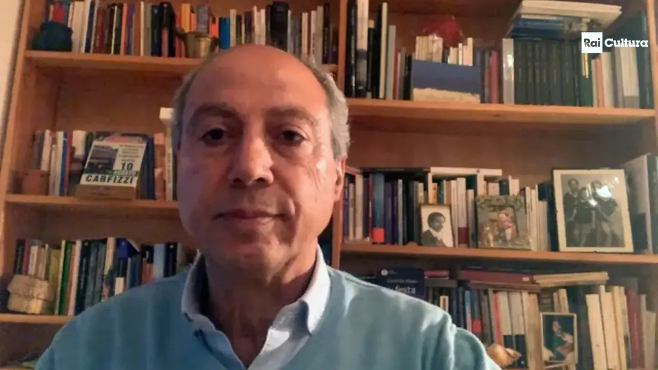 Carmine Abate, con libreria alle spalle, parla in videochiamata.