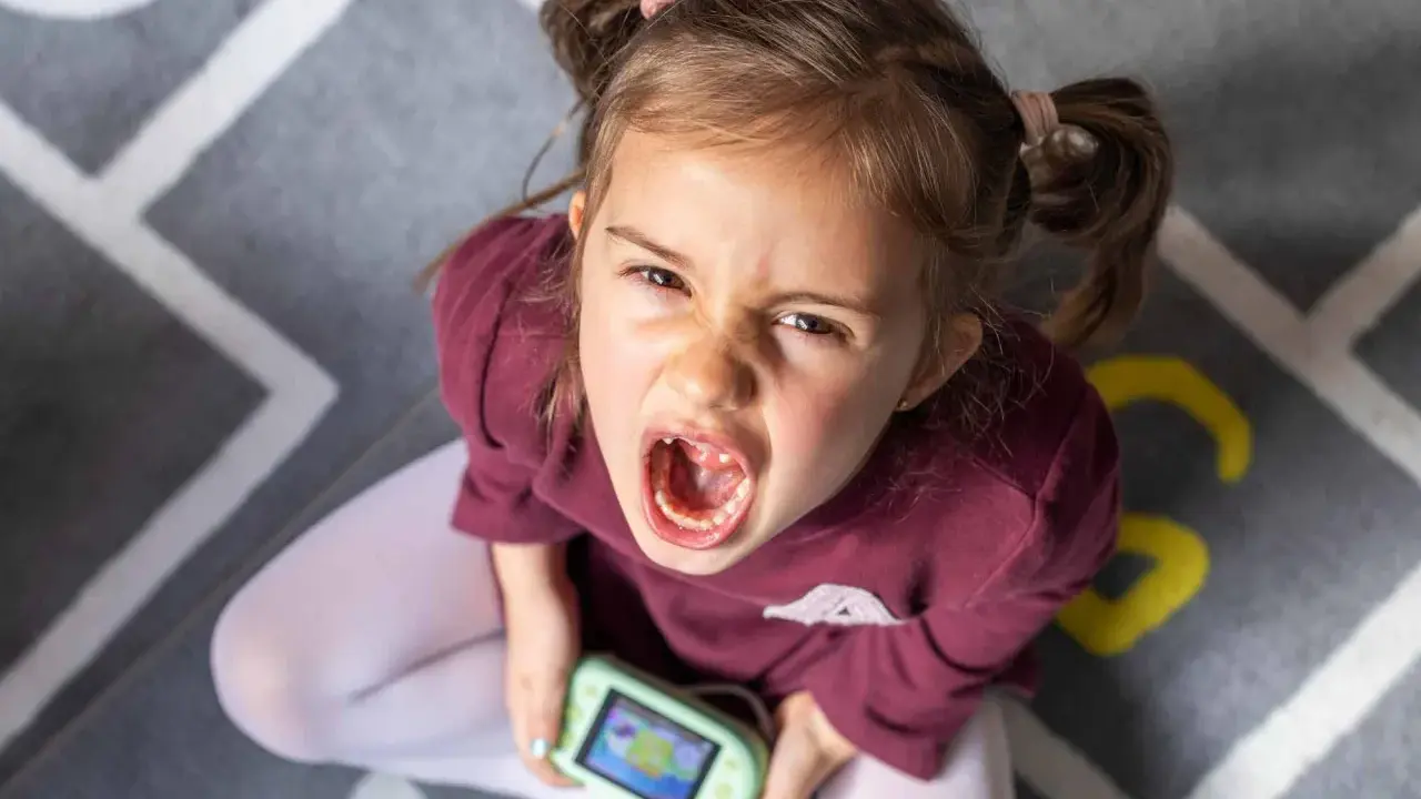 Niña con expresión de enfado y consola de videojuegos, un ejemplo de comportamiento disruptivo significado.