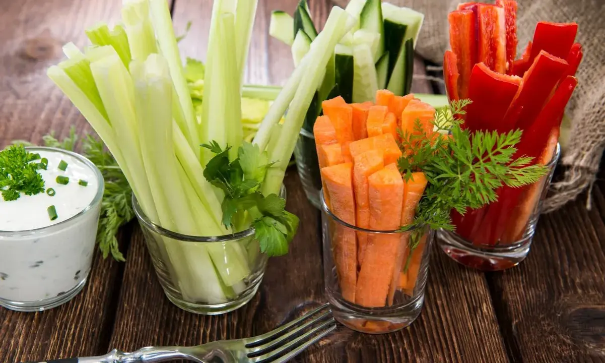 Geschnittene Karotten, Sellerie, Gurken und Paprika in Gläsern, dazu ein Dip. Perfekte Snacks nach dem Sport für gesunde Erholung.