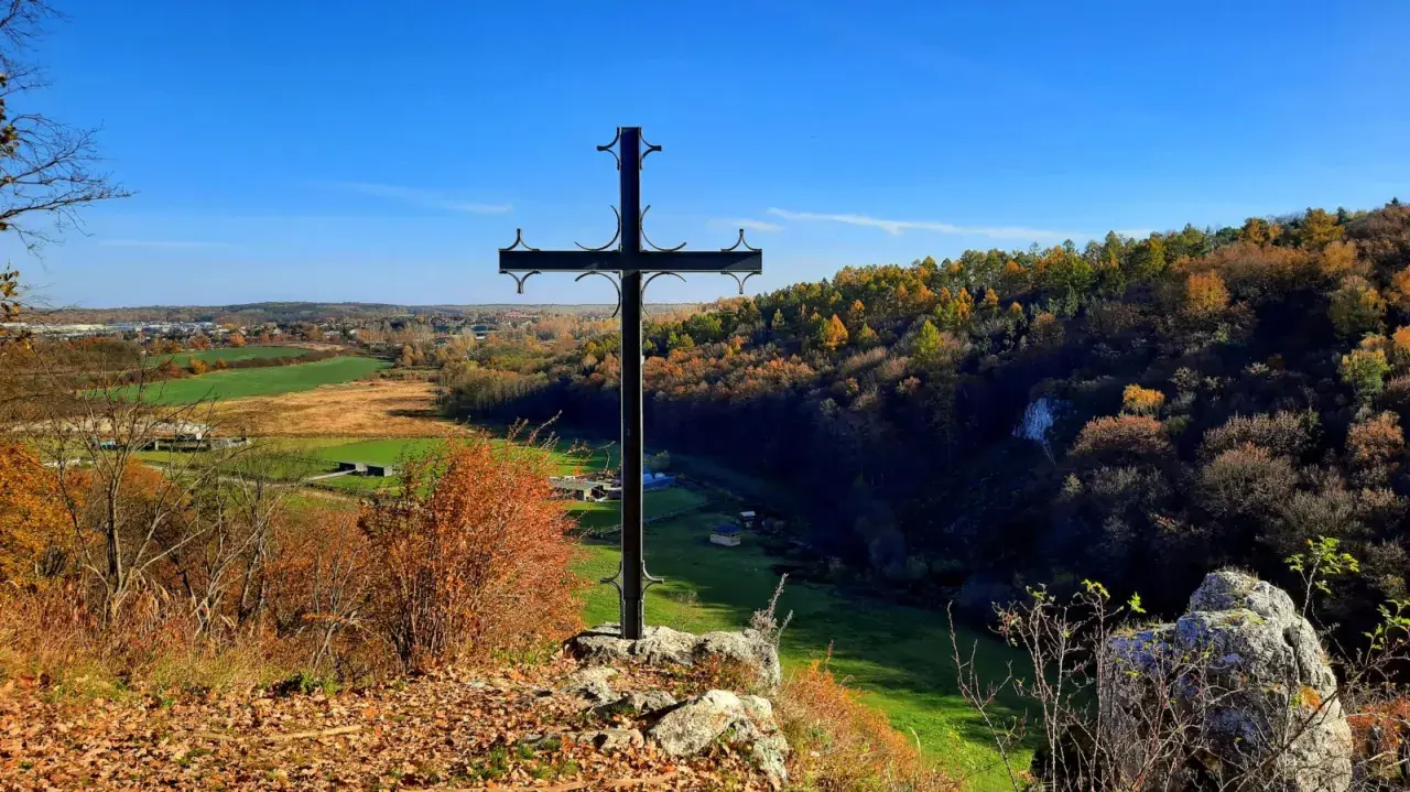 Czarny krzyż na skale góruje nad jesienną doliną Grzybowską. W oddali widać pola i lasy w barwach złota i czerwieni.