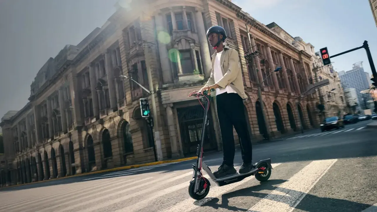 Un homme roule en trottinette électrique dans une rue bordée de bâtiments anciens. La taille roue trottinette semble adaptée à la ville.
