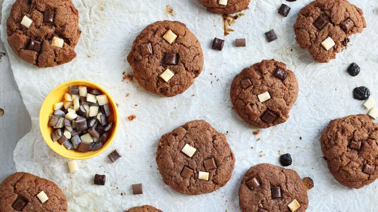 Gros plan sur des cookies au chocolat parsemés de morceaux de chocolat blanc et noir. Un petit bol jaune contient des morceaux de chocolat, comme un cookie stick.