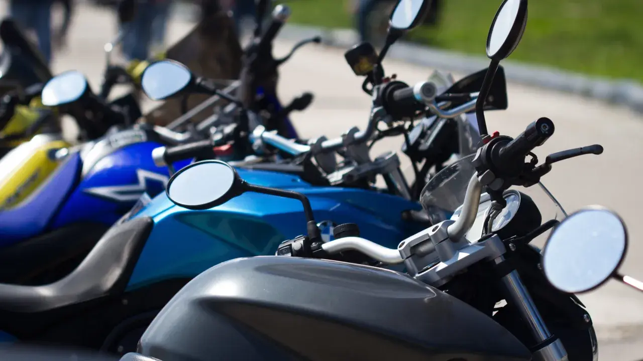 Manillar de moto con espejos y parte del depósito. Un carnet de moto a punto de ser usado.