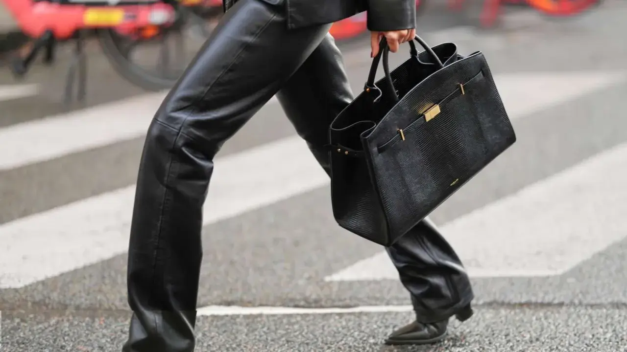 A person walks across a crosswalk in a chic leather pants outfit, perfect for winter. They carry a stylish black handbag.
