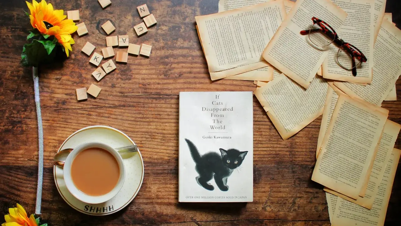 Libro "If Cats Disappeared From The World" con un gattino nero, occhiali, fiori e una tazza di tè. La trama esplora un mondo senza gatti.