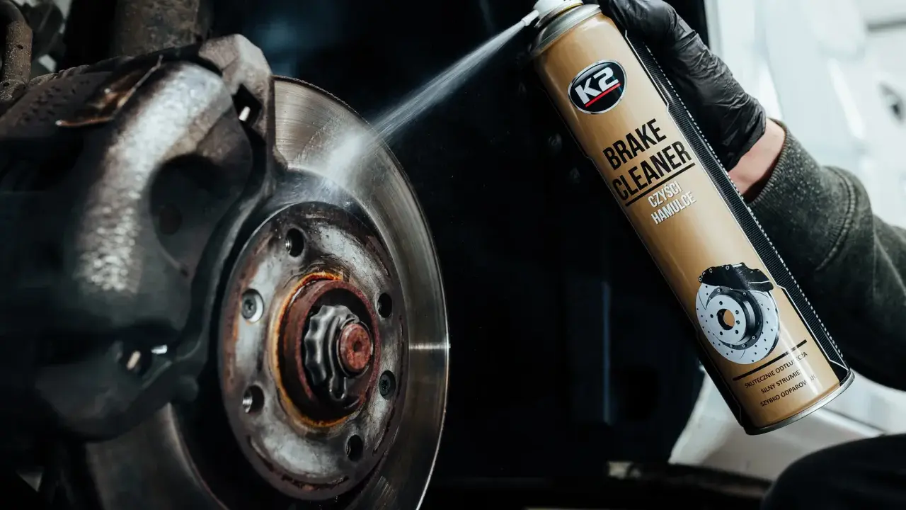 Ręka w czarnej rękawiczce rozpyla środek na zużyte tarcze hamulcowe. Preparat K2 Brake Cleaner skutecznie czyści hamulce.