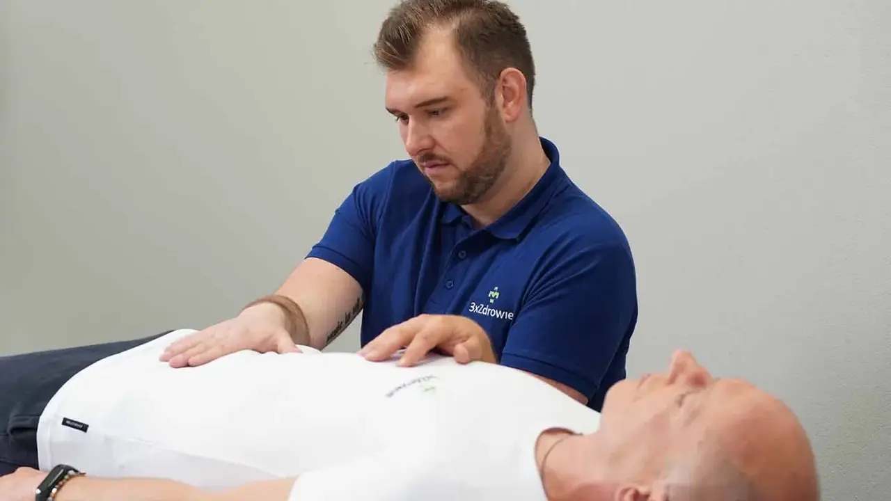 Terapeuta wykonuje zabieg z zakresu osteopatii wisceralnej, delikatnie dotykając brzucha pacjenta.