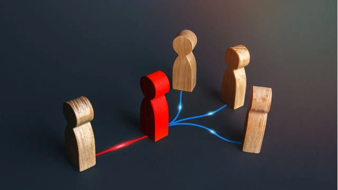 Figuras de madera conectadas por líneas de luz. Una figura roja central actúa como nodo, conectando a otras figuras, representando el papel de intermediarios financieros.