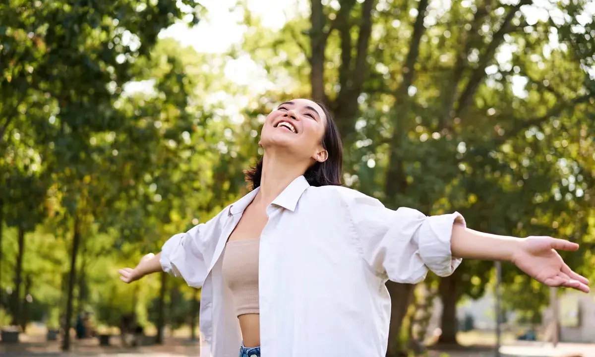 Jeune femme rayonnante dans un parc, profitant de la nature. Elle semble ressentir les bienfaits de la L-tyrosine pour son bien-être.