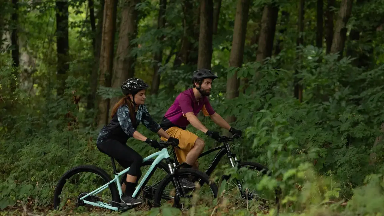 Para jadąca na rowerach górskich przez las. Czy to gravel, czy MTB? Trudno powiedzieć, ale zabawa jest przednia!