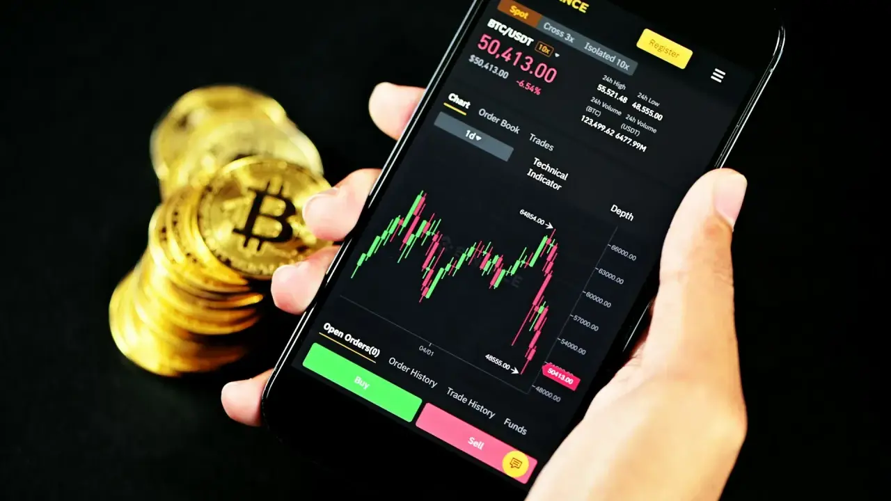 Ręka trzyma smartfon z wykresem kursu Bitcoina na platformie Binance. Obok stos złotych monet. Czy Binance czy Zonda? Decyzja należy do Ciebie.