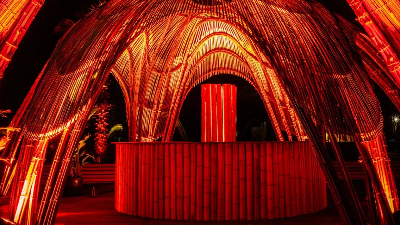 Struttura in bambù illuminata di rosso, con un bancone e un'installazione luminosa centrale. Atmosfera da house techno.