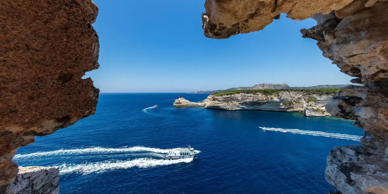 Blick durch Felsformationen auf das tiefblaue Meer bei Bonifacio, Korsika. Boote gleiten über die Wellen.