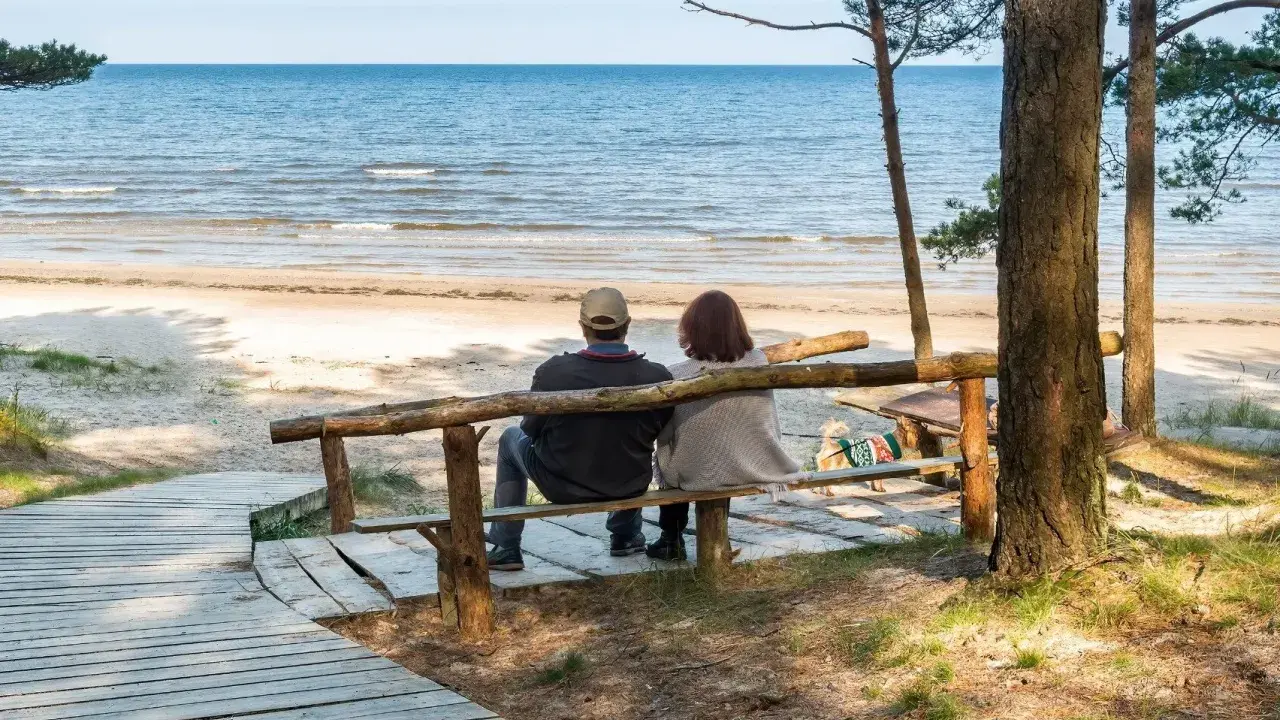 Para relaksująca para siedzi na ławce, patrząc na morze. Idealne miejsce na sanatoria nad morzem.