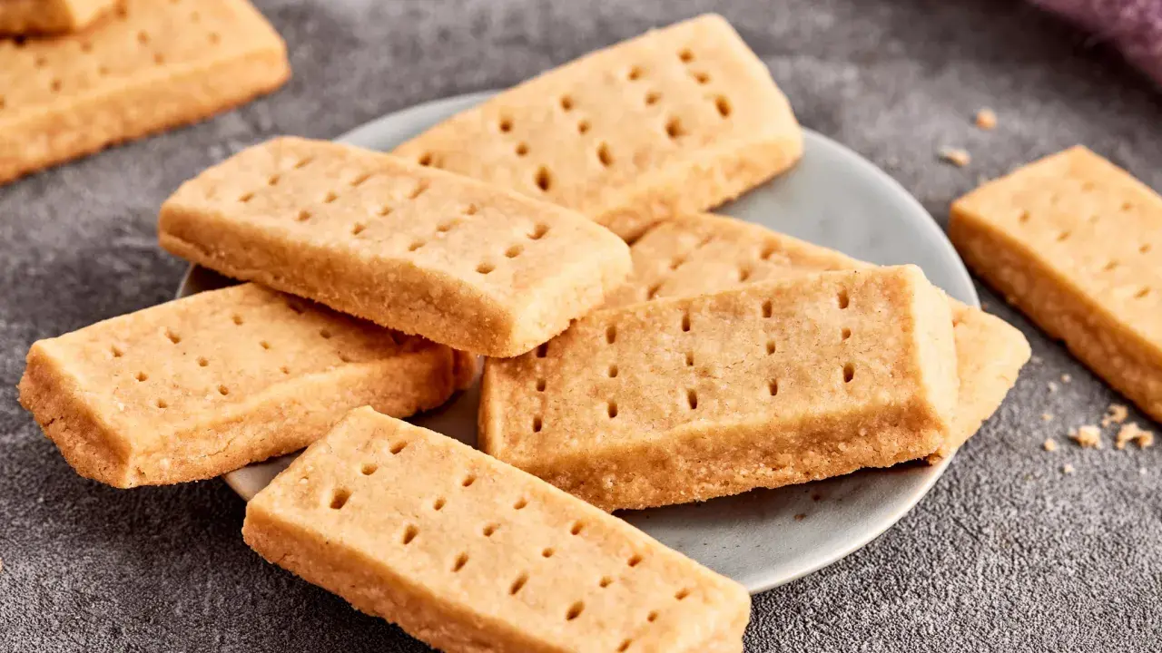 Goldbraune Shortbread-Kekse, perfekt für ein einfaches Shortbread Rezept. Sie liegen auf einem Teller und daneben ein lila Tuch.