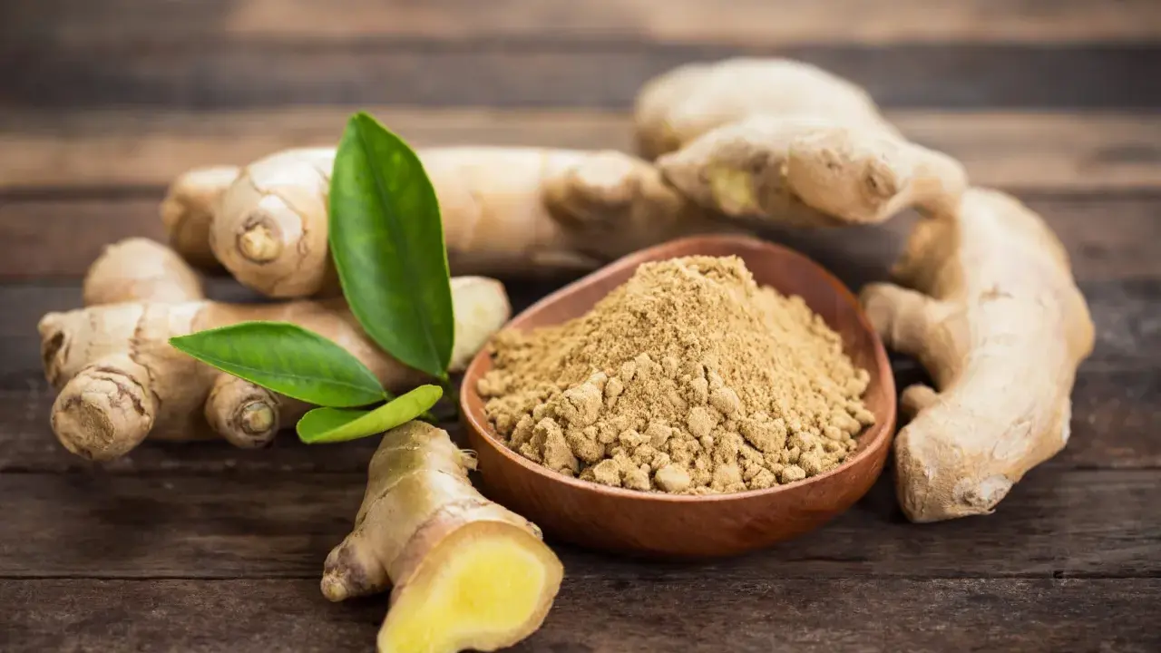 Des racines de gingembre frais et de la poudre de gingembre dans un bol en bois. Le gingembre est-il aphrodisiaque ? Une question qui suscite la curiosité.