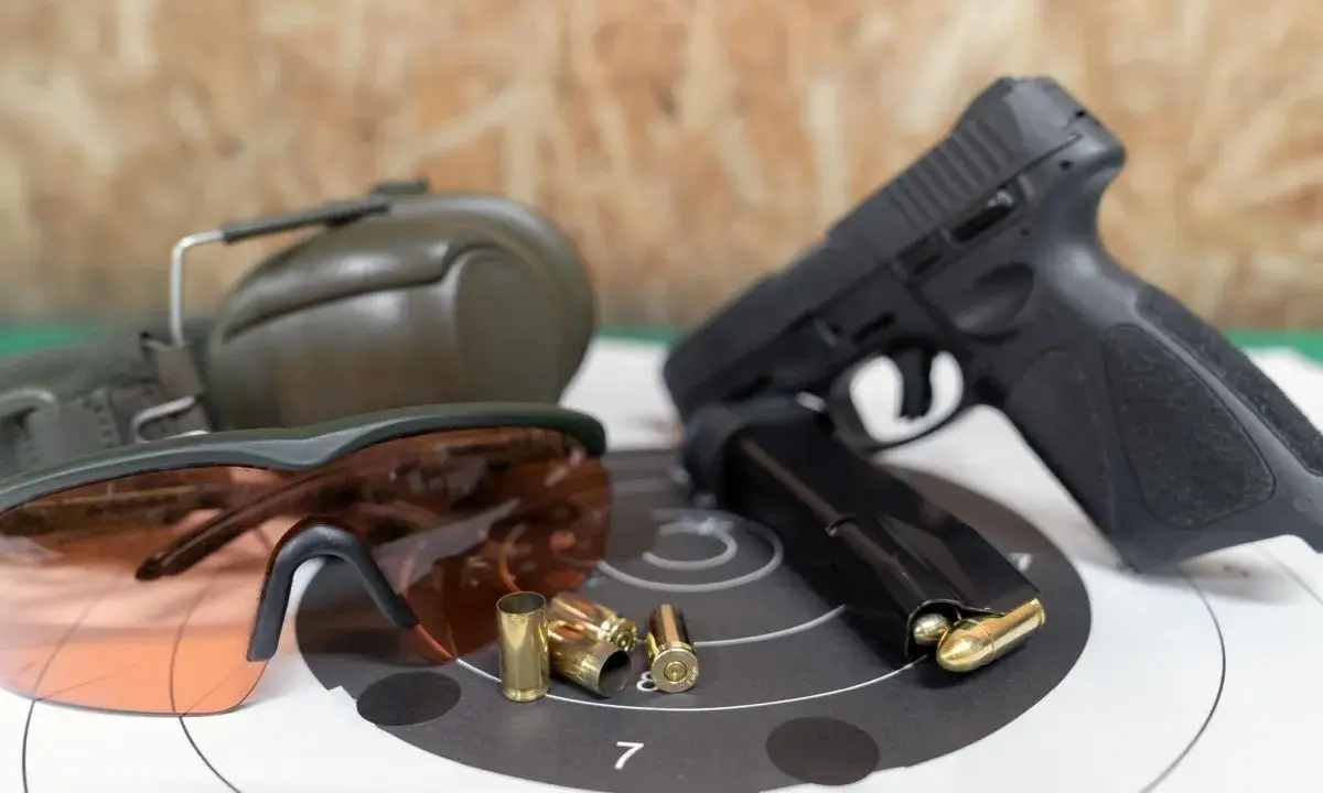 Pistolet, magazynek, łuski, okulary ochronne i słuchawki – kompletne akcesoria strzeleckie gotowe do użycia.