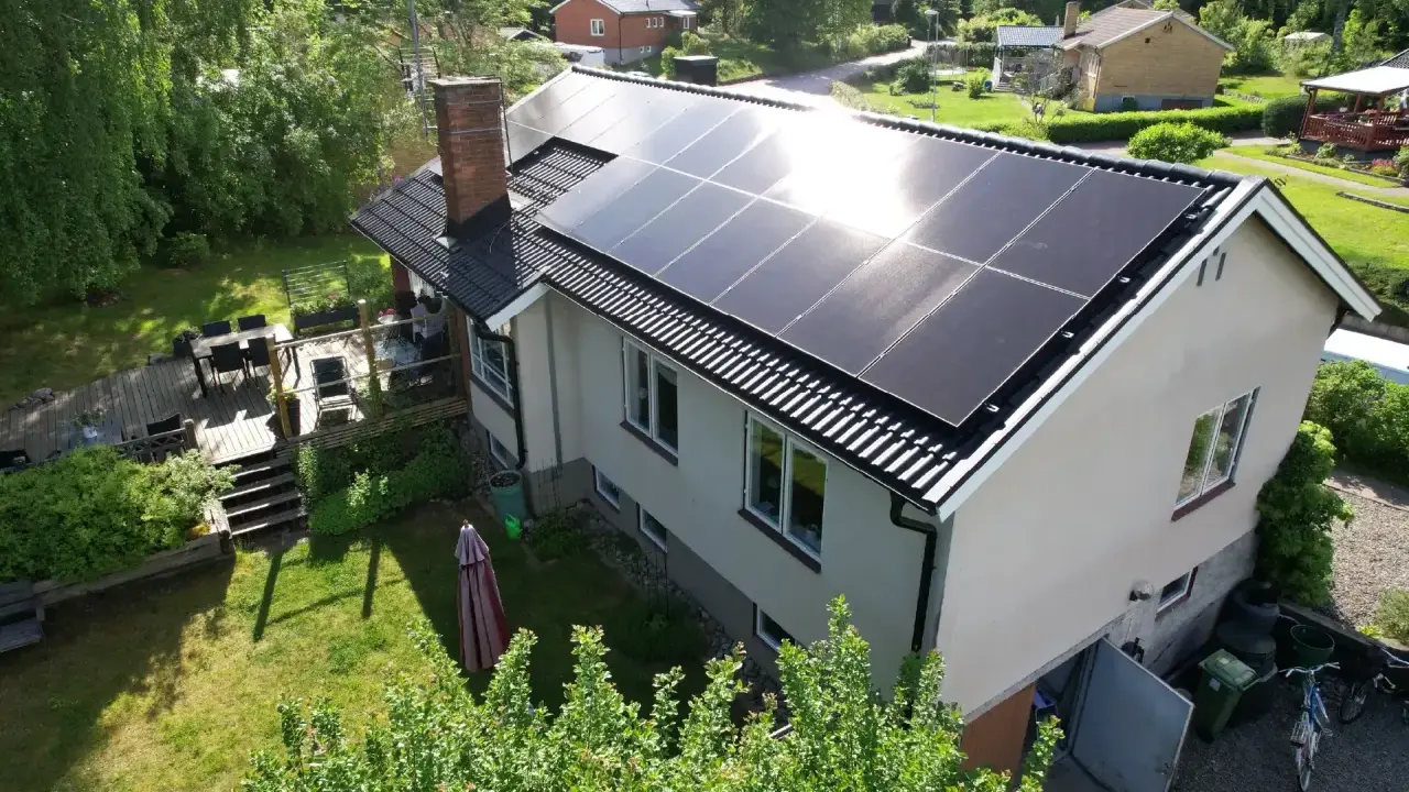 Ett hus med solpaneler på taket, redo att fånga solens energi. En grönskande trädgård och en altan inbjuder till avkoppling.
