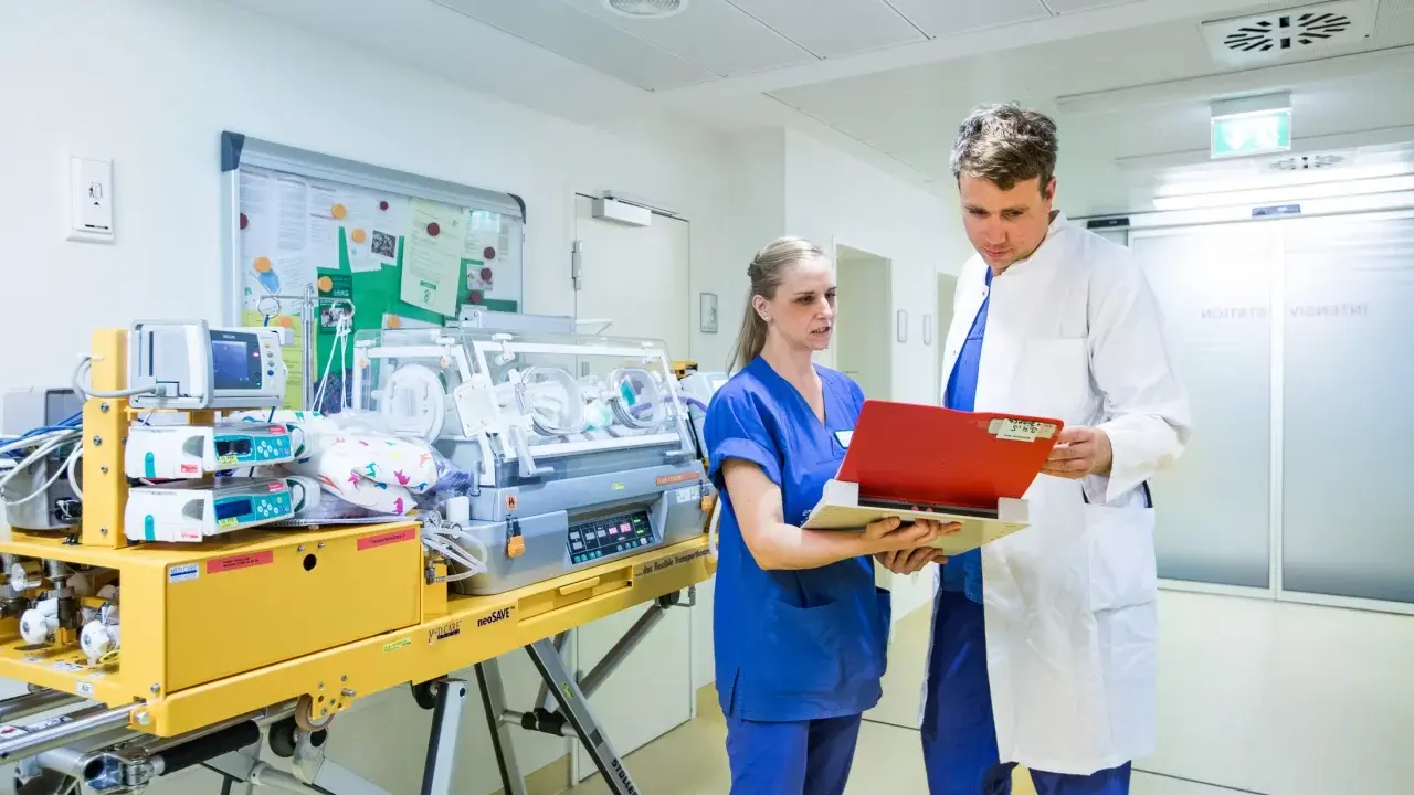 Personale medico discute in terapia intensiva neonatale accanto a un'incubatrice.