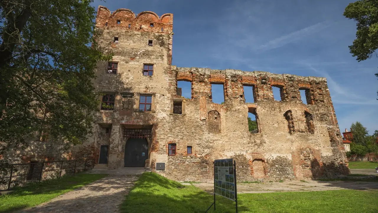 Zamek w Ząbkowicach Śląskich, ruiny z ceglaną wieżą i bramą, otoczone zielenią i błękitnym niebem.
