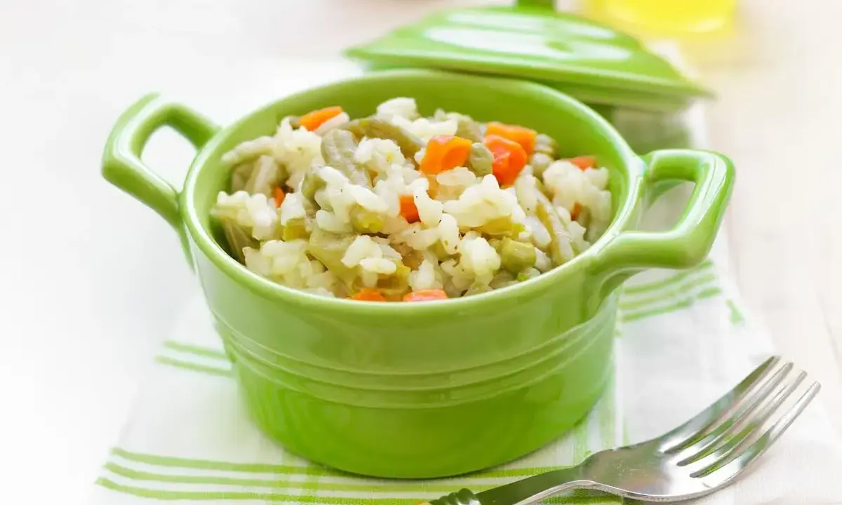 Un tazón verde vibrante lleno de arroz con verduras para bebé, con zanahorias y guisantes.