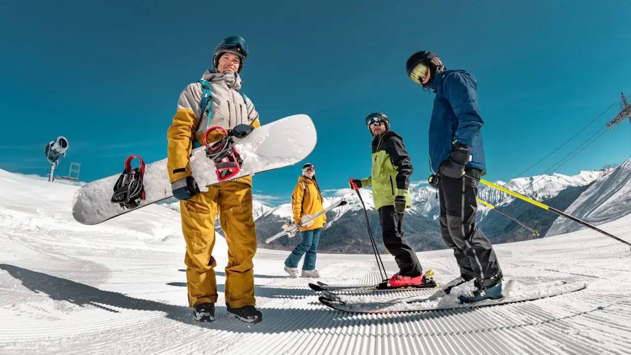 Grupa narciarzy i snowboardzistów na ośnieżonym stoku z widokiem na góry.