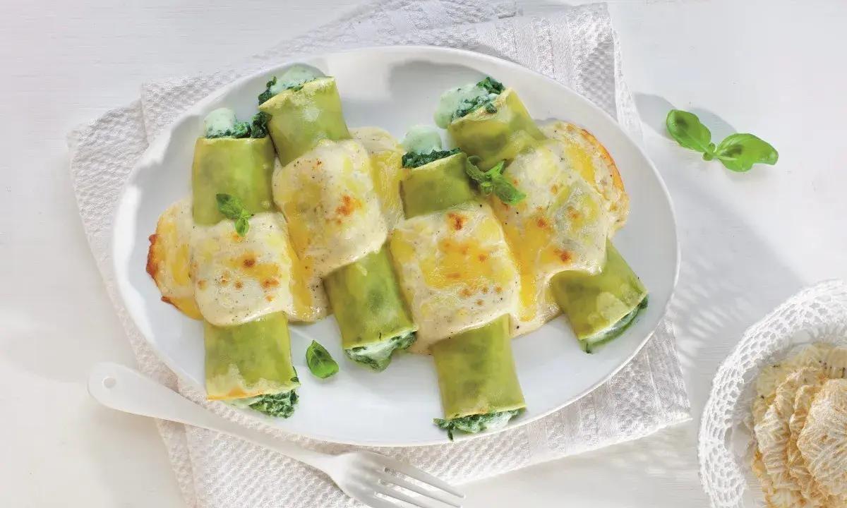 Zielone cannelloni ze szpinakiem, zapieczone pod kremowym sosem serowym, ozdobione listkami bazylii.