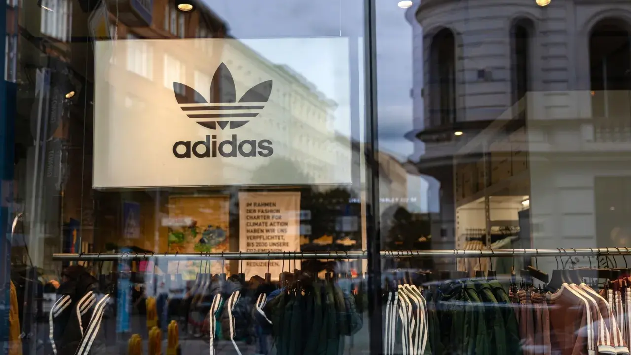Witryna sklepu z logo adidas, marki pochodzącej z Niemiec. Wieszaki z ubraniami, w tym kurtki i bluzy z charakterystycznymi trzema paskami.