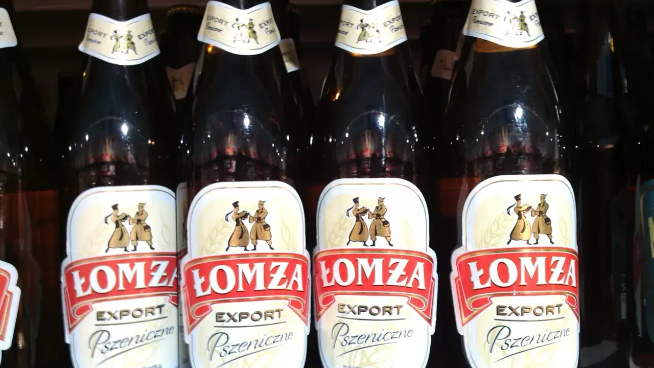 Butelki piwa Łomża Export Pszeniczne w rzędzie. Etykiety z postaciami i kłosem zboża.