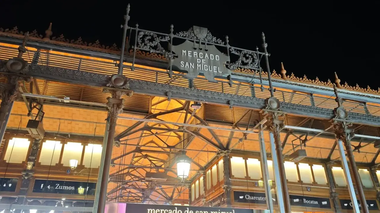 Das Mercado de San Miguel bei Nacht, mit seinem verzierten Eingang und den Lichtern, die durch das Glasdach scheinen.