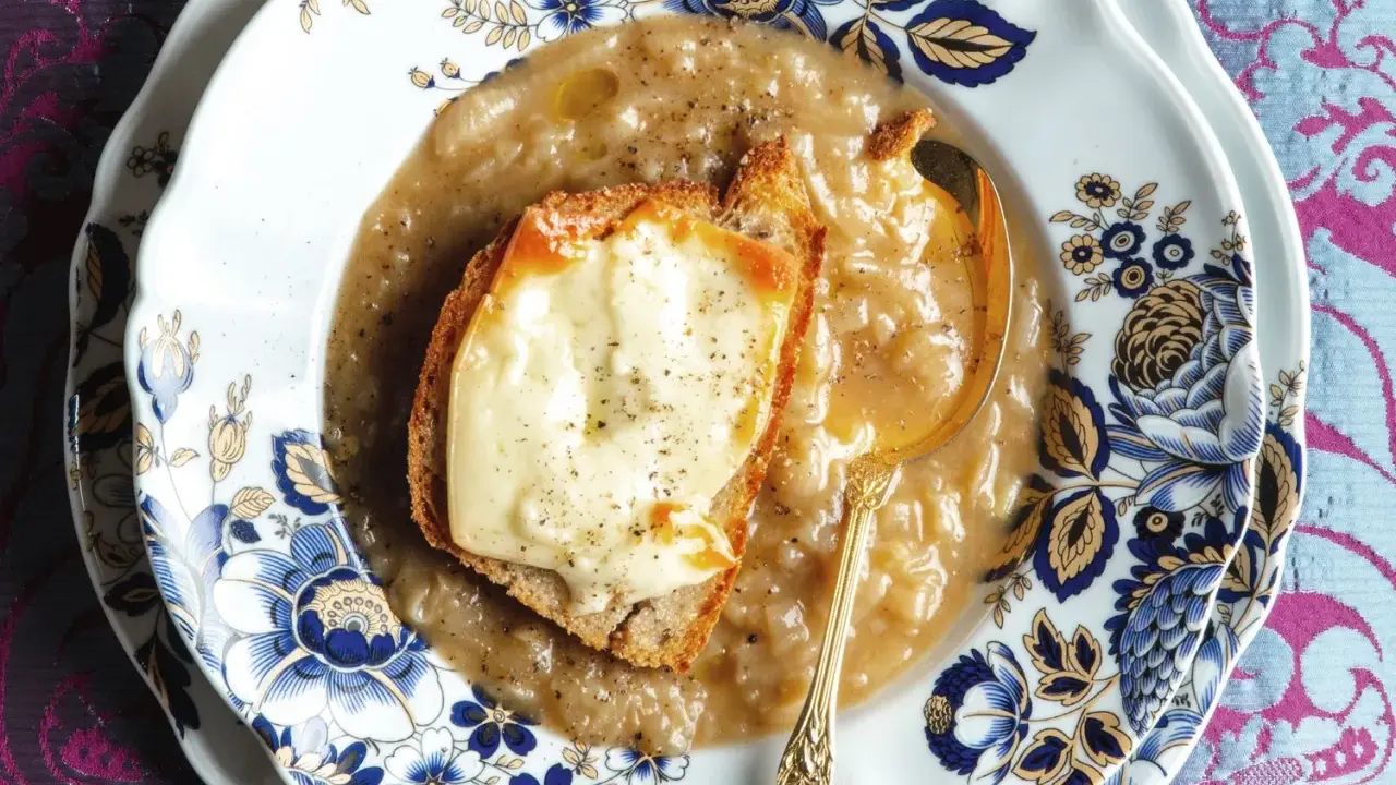 Piatto di zuppa di cipolle fumante, con crostino di pane e formaggio fuso, servita su un elegante piatto decorato.