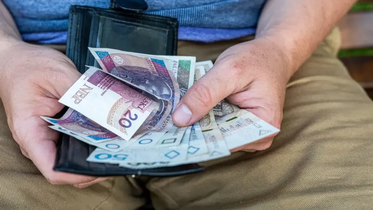 Dłonie trzymają portfel z polskimi banknotami. To może być kwota na zasilek pielegnacyjny.