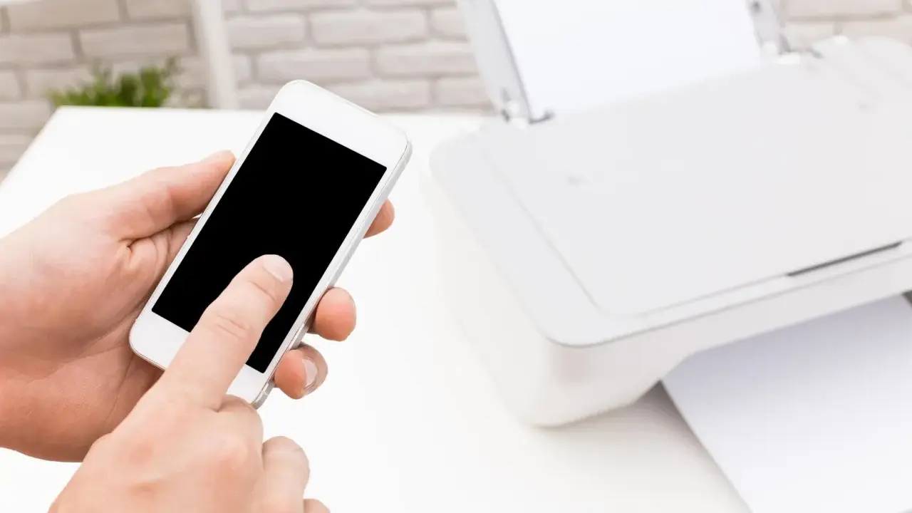 Instrukcja: jak połączyć telefon z drukarką. Smartfon w dłoni, obok drukarka z papierem.