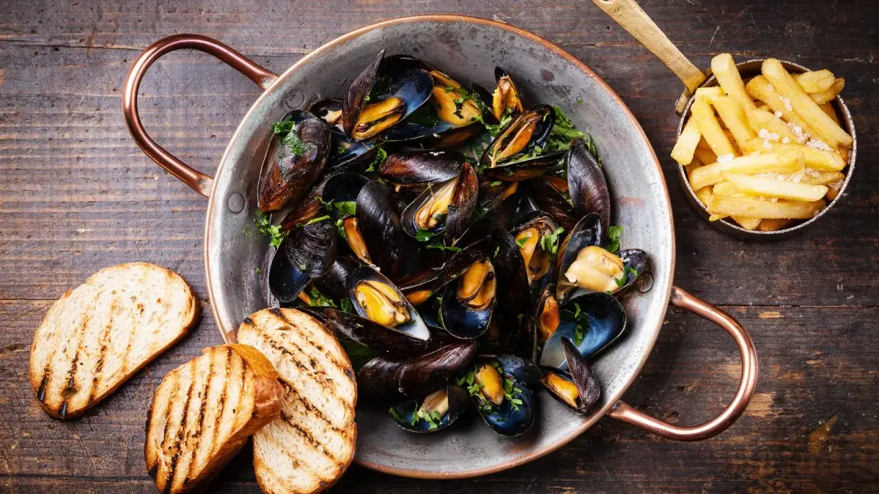 Moules marinières, une spécialité culinaire normande, servies dans une marmite en cuivre avec des frites et du pain grillé.
