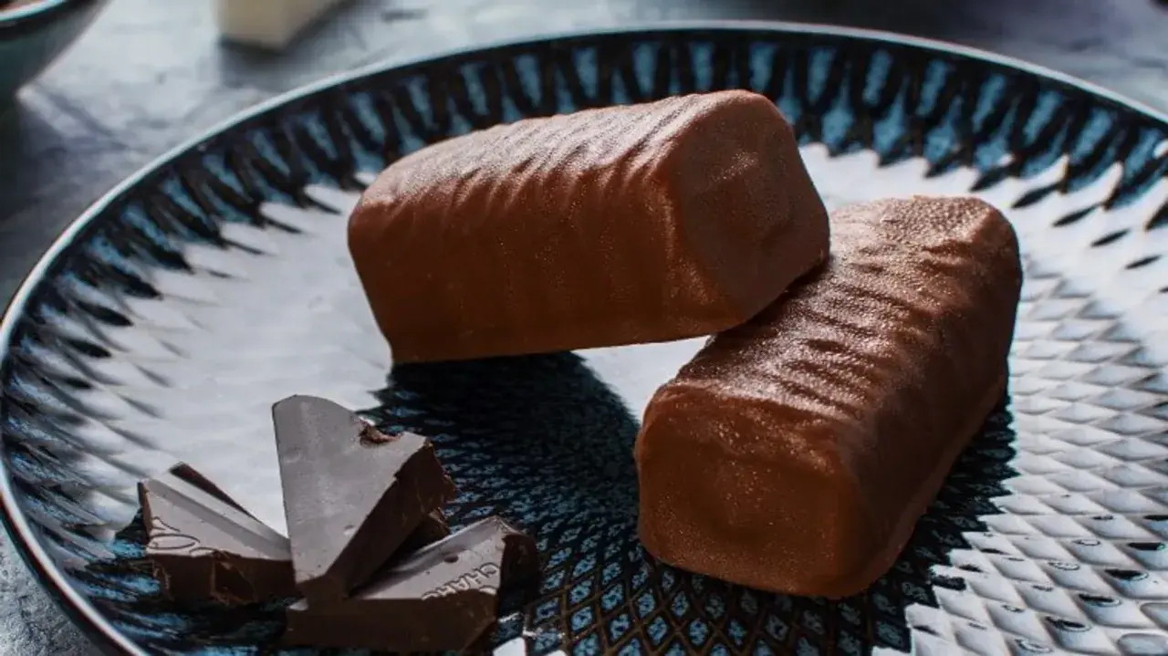Dwa czekoladowe batony proteinowe na talerzu, obok kawałki gorzkiej czekolady. Idealne do domowego batony proteinowe przepis.