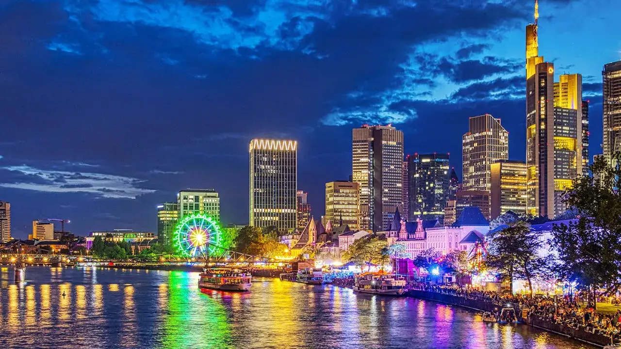 Frankfurt Mainufer bei Nacht: Lichtermeer, beleuchtetes Riesenrad und Skyline spiegeln sich im Wasser.